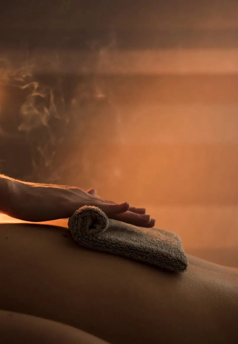 A warm towel is laid across a client's back in a steam-lit room.