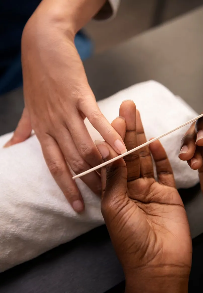 A technician files a client's nails over a folded towel.
